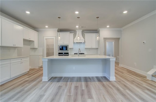 kitchen featuring an island with sink, a sink, custom range hood, wall oven, and stainless steel microwave