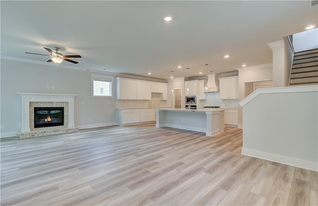 unfurnished living room with stairs, baseboards, light wood-style floors, and crown molding