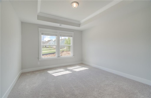 carpeted spare room with a tray ceiling, visible vents, baseboards, and ornamental molding