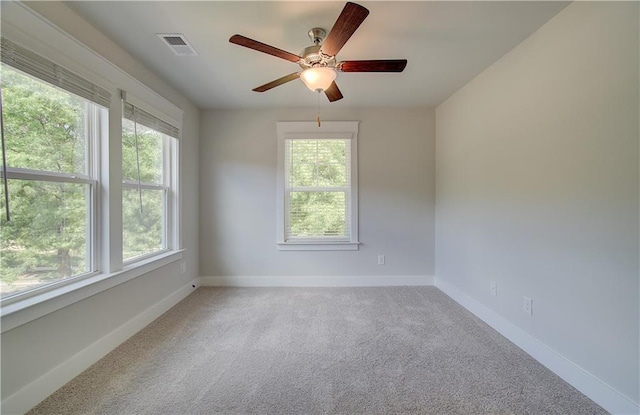 empty room featuring visible vents, light colored carpet, a ceiling fan, and baseboards