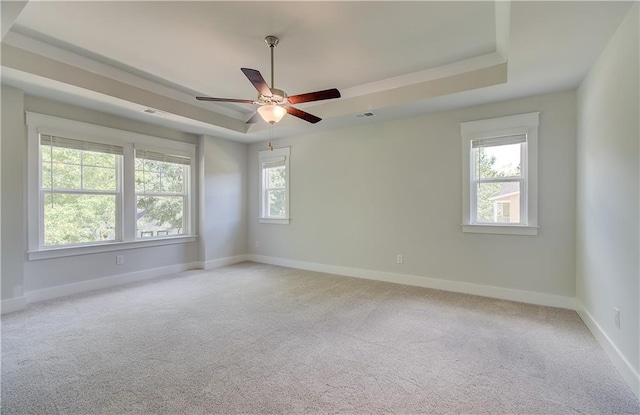 empty room with a ceiling fan, visible vents, baseboards, a tray ceiling, and light colored carpet