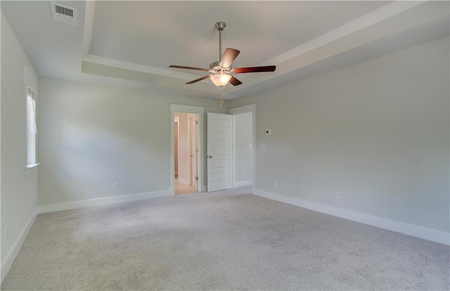 carpeted empty room with visible vents, ceiling fan, a raised ceiling, and baseboards