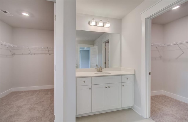 bathroom with a spacious closet, visible vents, vanity, and baseboards