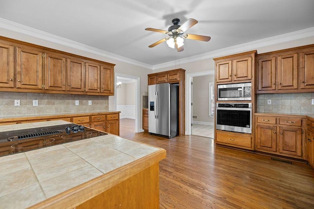 kitchen with crown molding, stainless steel appliances, tile counters, and backsplash