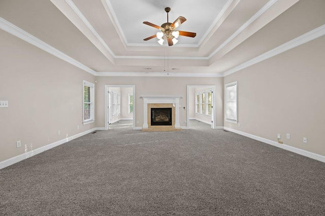 unfurnished living room with crown molding, ceiling fan, a raised ceiling, and a wealth of natural light