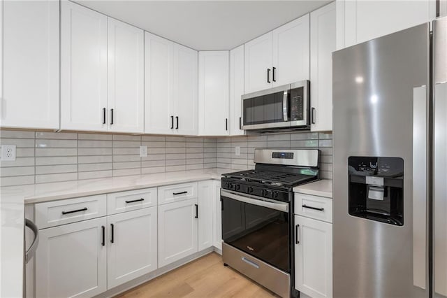 1409 Georgia Ave, East Point, GA 30344 - kitchen featuring appliances with stainless steel finishes, white cabinetry, light wood finished floors, tasteful backsplash, and light stone counters