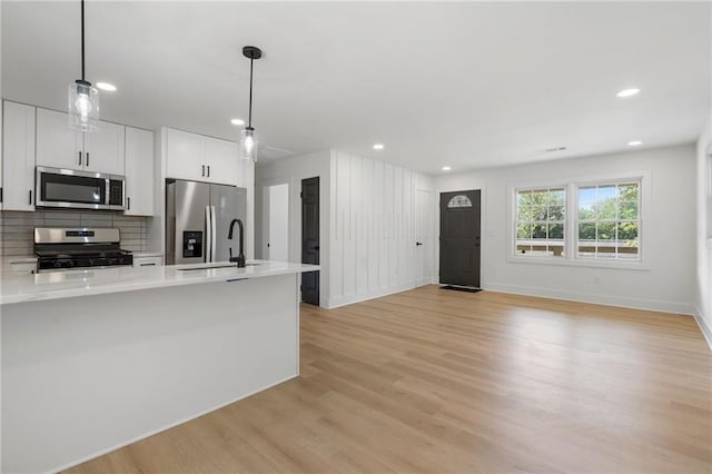 1409 Georgia Ave, East Point, GA 30344 - kitchen featuring appliances with stainless steel finishes, light countertops, light wood-type flooring, decorative backsplash, and pendant lighting