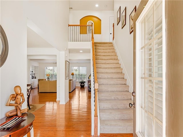 foyer entrance with stairway, baseboards, light wood-style floors, and a towering ceiling