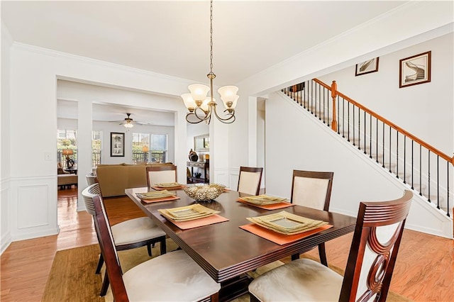 dining room featuring stairway, ornamental molding, wainscoting, light wood-style flooring, and a decorative wall