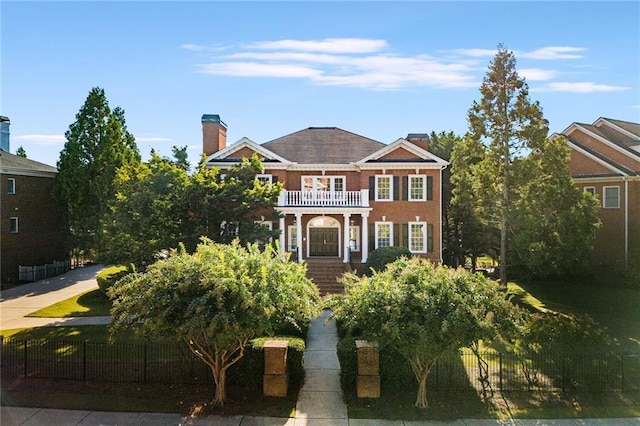 georgian-style home with a balcony, a fenced front yard, and brick siding