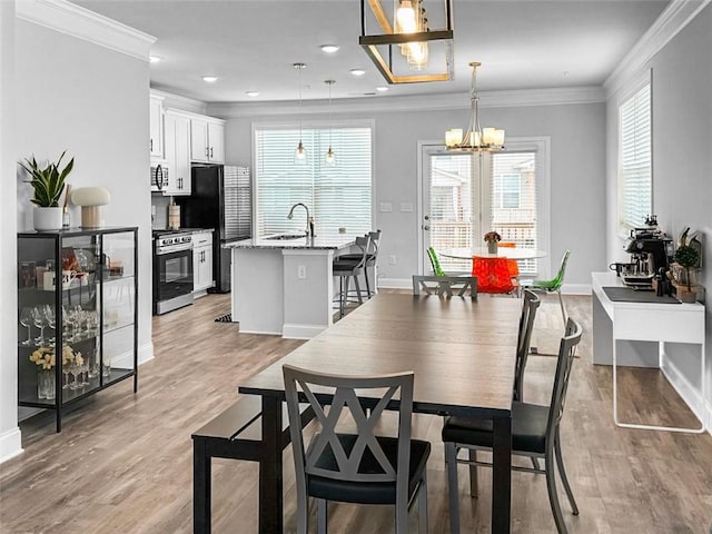 dining room featuring sink, ornamental molding, light hardwood / wood-style flooring, and an inviting chandelier