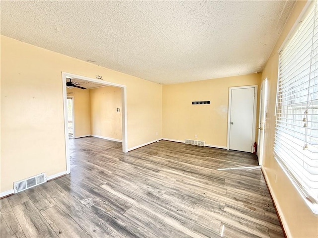 empty room with visible vents, baseboards, a textured ceiling, and wood finished floors