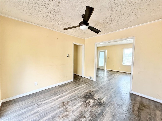 empty room with visible vents, a textured ceiling, wood finished floors, and ornamental molding