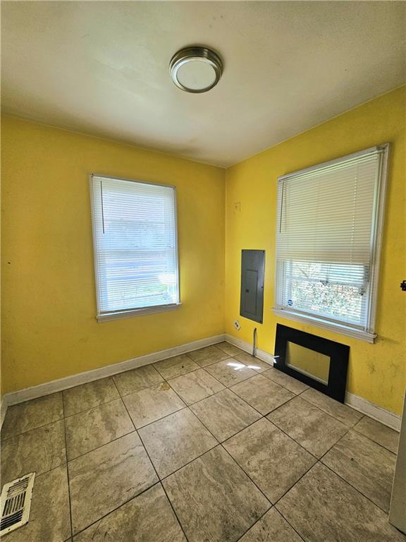 unfurnished room with a wealth of natural light, visible vents, tile patterned floors, and electric panel