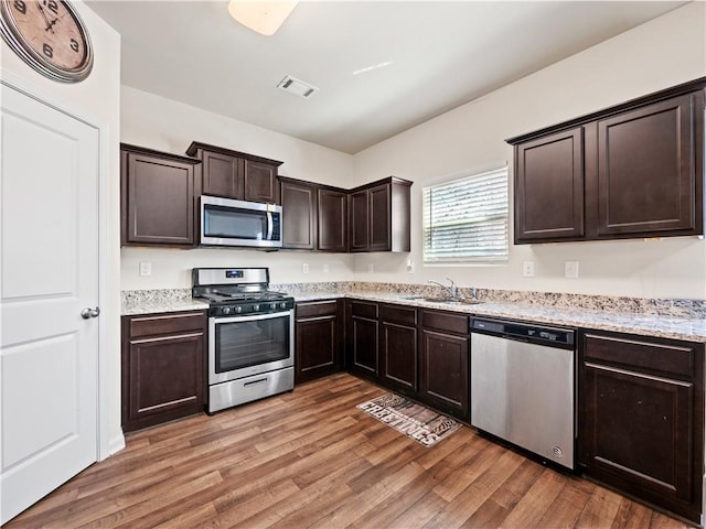 kitchen featuring light wood-style flooring, dark brown cabinetry, a sink, visible vents, and appliances with stainless steel finishes