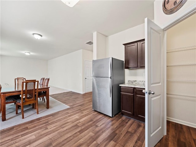 kitchen featuring dark wood-style flooring, visible vents, baseboards, dark brown cabinets, and freestanding refrigerator