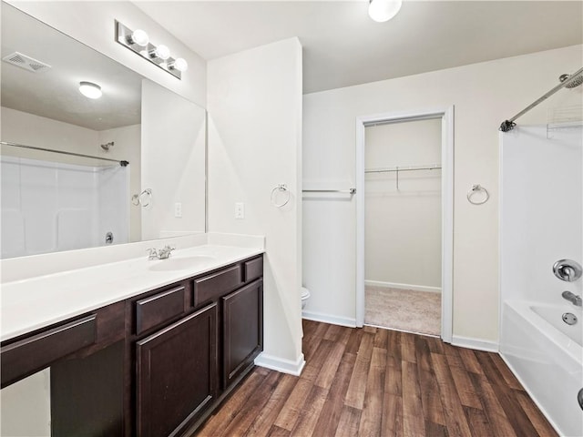 bathroom featuring toilet, wood finished floors, visible vents, baseboards, and washtub / shower combination