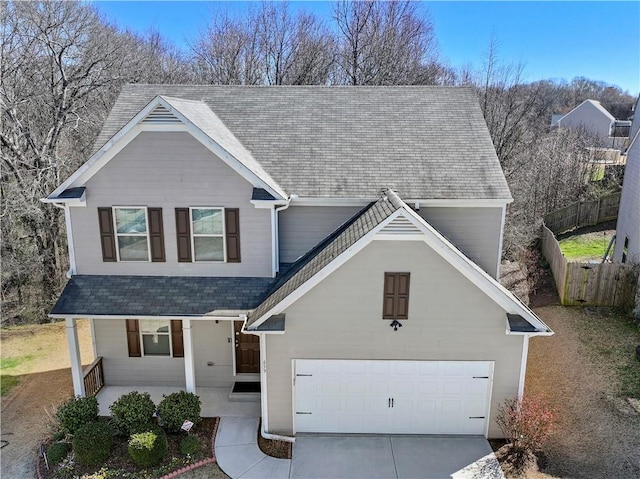 traditional-style home with concrete driveway, a porch, a shingled roof, and fence