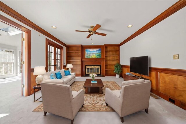 carpeted living room featuring ceiling fan, built in features, wood walls, and ornamental molding