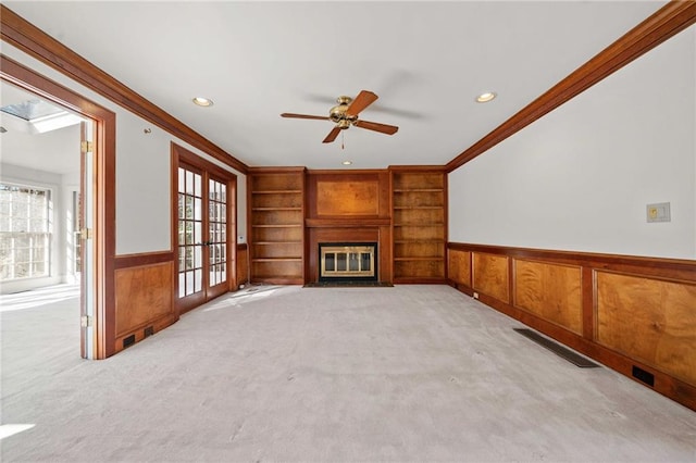 unfurnished living room with ceiling fan, a fireplace, crown molding, and light carpet