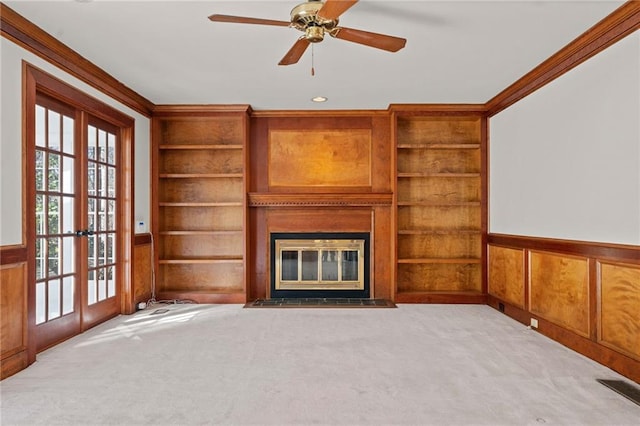 unfurnished living room with built in shelves, french doors, light colored carpet, and ornamental molding