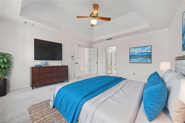 carpeted bedroom with a tray ceiling, ensuite bath, and ceiling fan