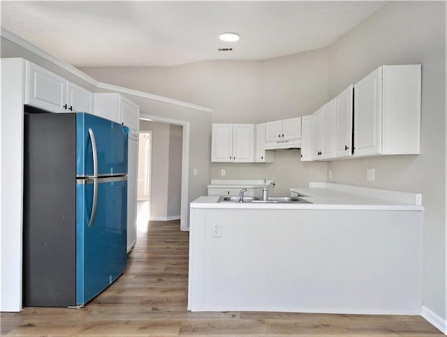 kitchen with lofted ceiling, freestanding refrigerator, white cabinets, a sink, and a peninsula