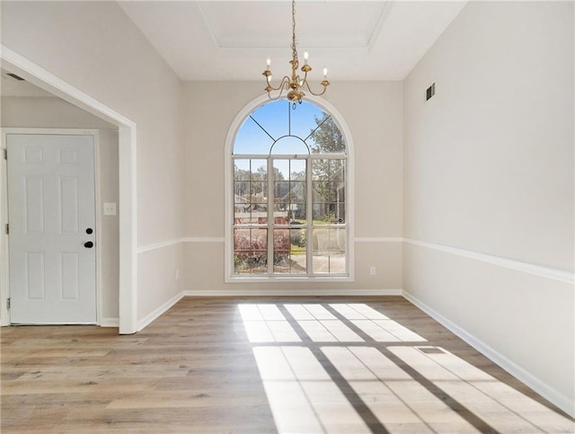 unfurnished dining area featuring a raised ceiling, a notable chandelier, baseboards, and wood finished floors