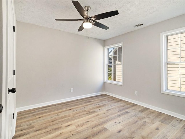 spare room with light wood-style floors, baseboards, visible vents, and a textured ceiling