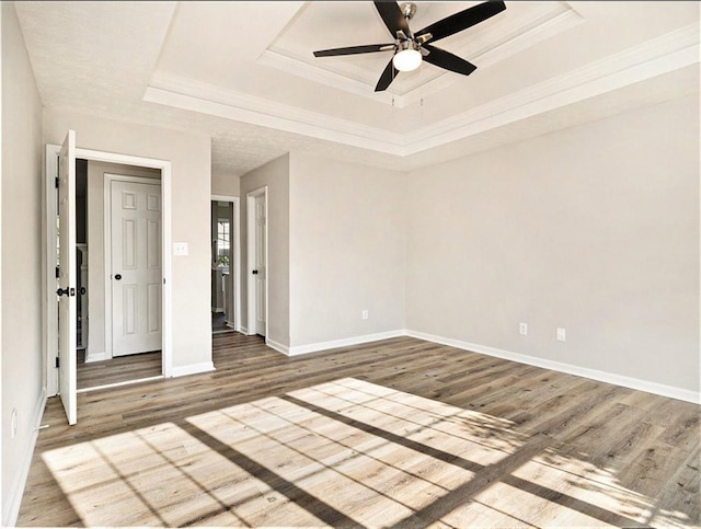 empty room featuring ornamental molding, a raised ceiling, baseboards, and wood finished floors