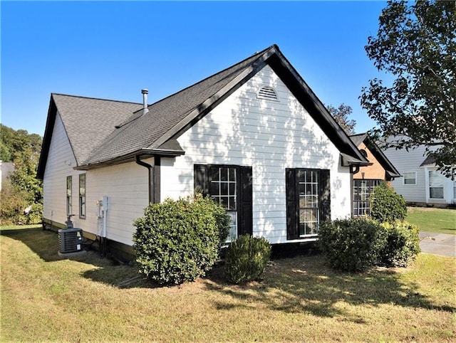 rear view of house featuring a shingled roof, a lawn, and central AC unit