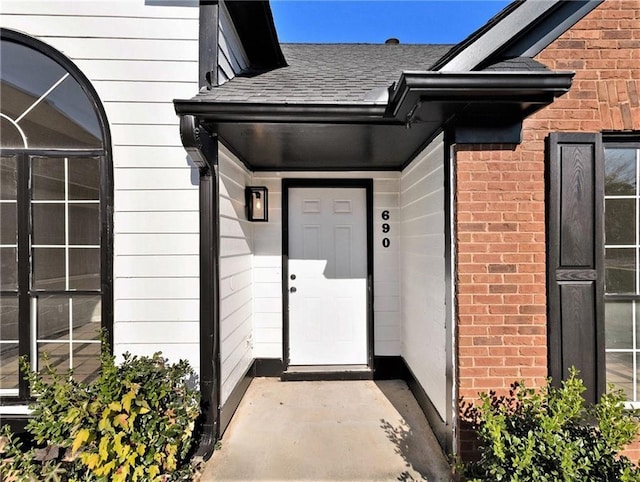 entrance to property with a shingled roof and brick siding