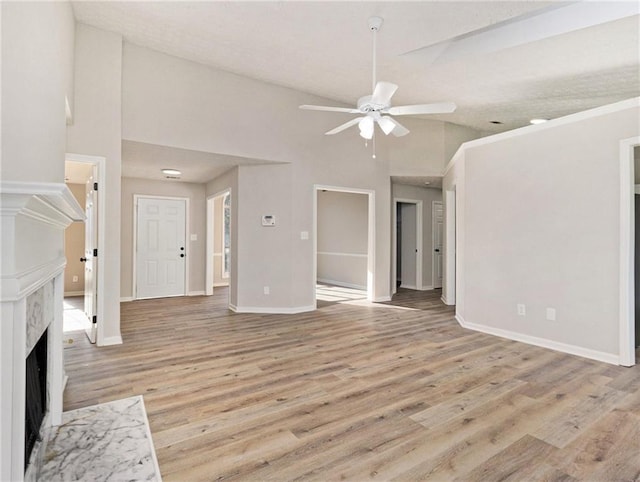 unfurnished living room featuring light wood finished floors, a premium fireplace, ceiling fan, high vaulted ceiling, and baseboards