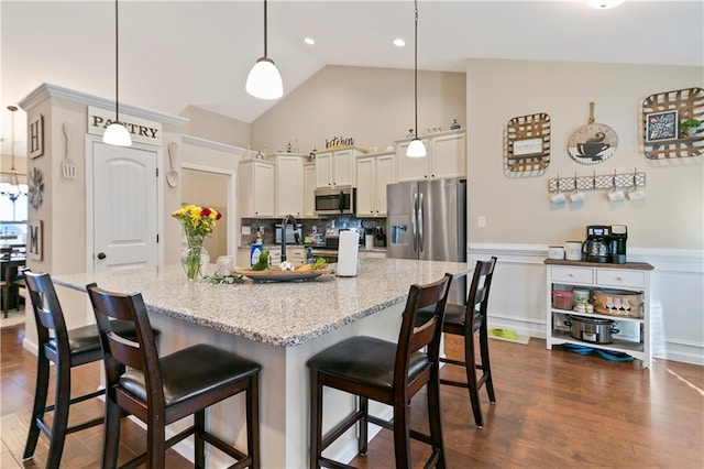 kitchen with dark wood-style flooring, a kitchen breakfast bar, appliances with stainless steel finishes, backsplash, and decorative light fixtures