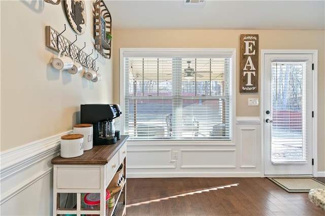 doorway to outside featuring a wainscoted wall, visible vents, a decorative wall, and dark wood-type flooring