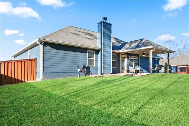 rear view of property featuring a chimney, ceiling fan, fence, and a lawn