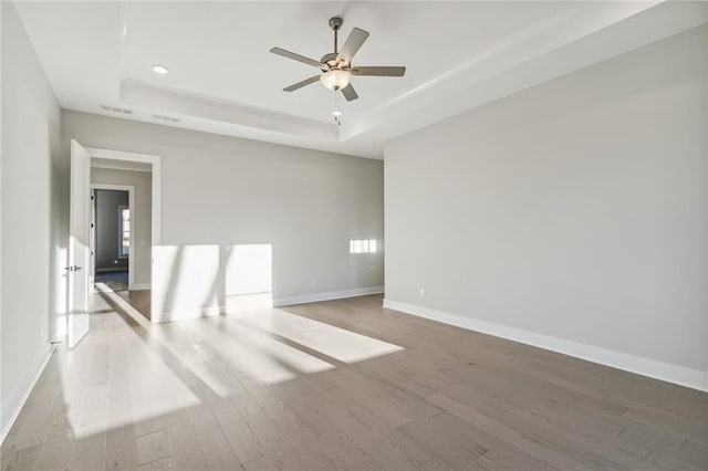 empty room with a tray ceiling, ceiling fan, and light wood-type flooring