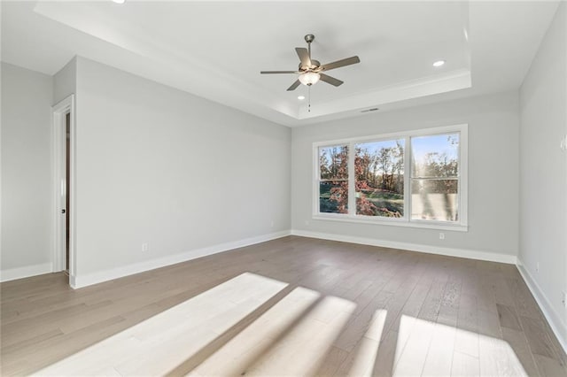 empty room featuring ceiling fan, a raised ceiling, and light hardwood / wood-style flooring