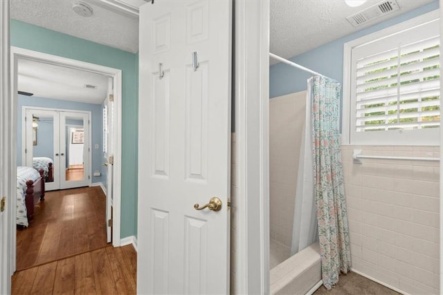 bathroom with hardwood / wood-style floors, a textured ceiling, tile walls, french doors, and curtained shower