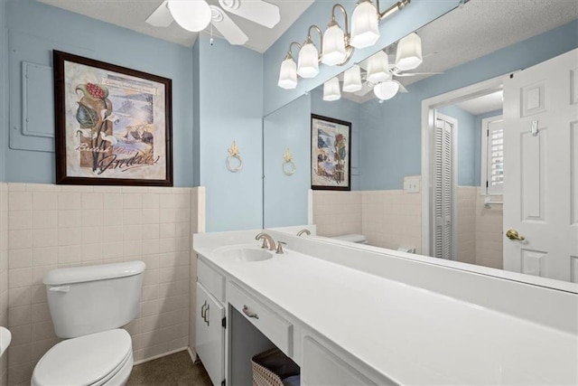 bathroom featuring a textured ceiling, toilet, ceiling fan, tile walls, and vanity