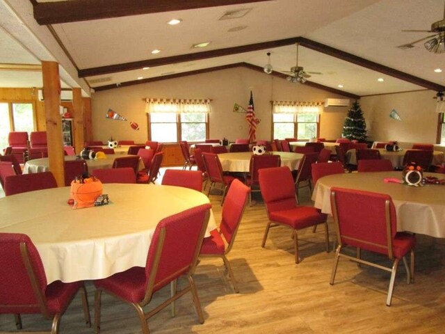 dining space featuring hardwood / wood-style flooring, a wall mounted AC, ceiling fan, and vaulted ceiling with beams