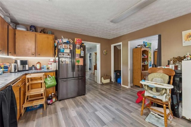 151 Grandma Branch Rd, Grantville, GA 30220 - kitchen featuring brown cabinetry, light wood-style floors, a textured ceiling, and freestanding refrigerator