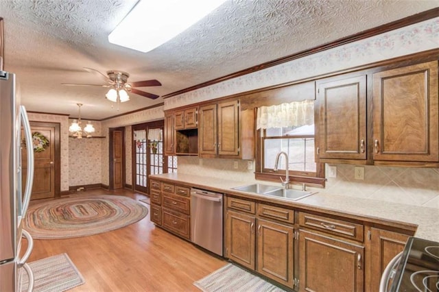 kitchen featuring sink, decorative light fixtures, light hardwood / wood-style flooring, ornamental molding, and appliances with stainless steel finishes