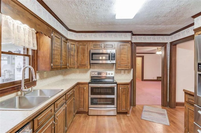 kitchen featuring sink, light wood-type flooring, ornamental molding, and appliances with stainless steel finishes