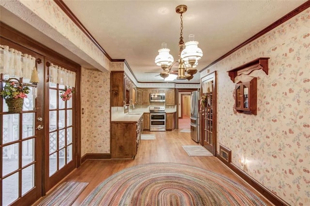 interior space with crown molding, appliances with stainless steel finishes, an inviting chandelier, french doors, and light wood-type flooring