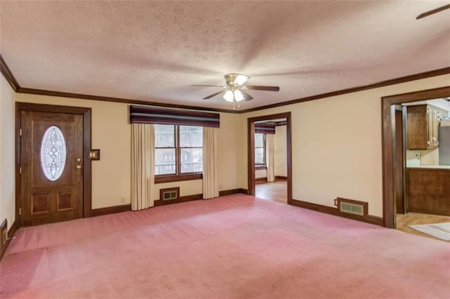 carpeted foyer entrance featuring ceiling fan, ornamental molding, and a textured ceiling