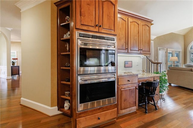 kitchen featuring ornamental molding, light stone countertops, dark hardwood / wood-style floors, and stainless steel double oven