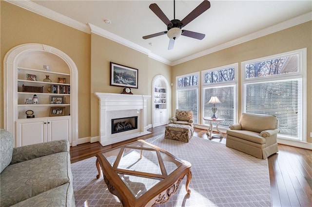 living room featuring hardwood / wood-style floors, built in features, ornamental molding, ceiling fan, and a high end fireplace