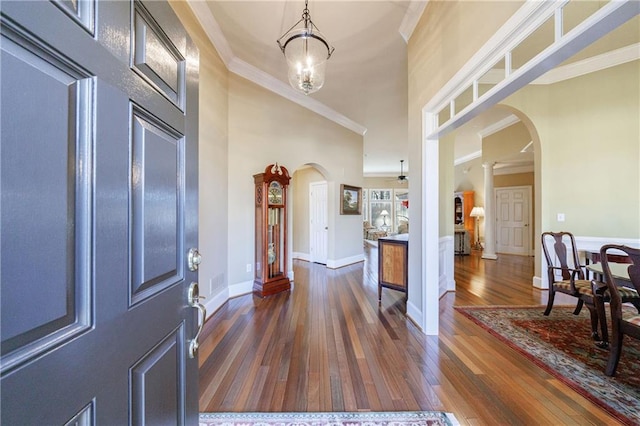 entryway featuring a towering ceiling, ornamental molding, dark hardwood / wood-style floors, and ceiling fan with notable chandelier