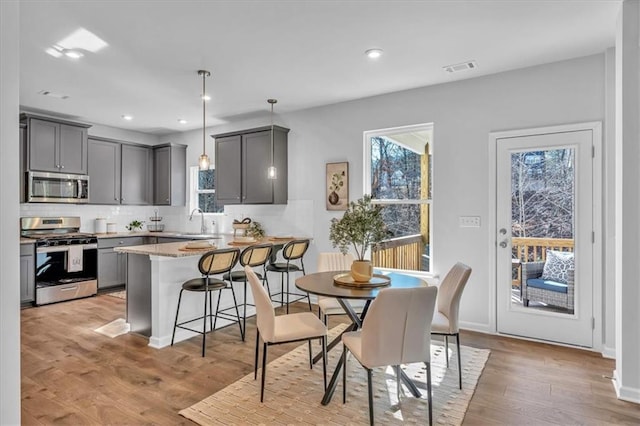 interior space with a kitchen bar, sink, gray cabinetry, pendant lighting, and stainless steel appliances